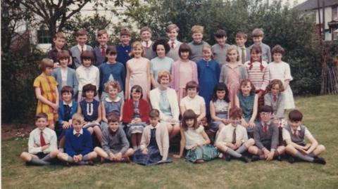 A 1966 colour image of Miss Arnold's class at Loose Primary School in Kent standing and sitting in four rows 