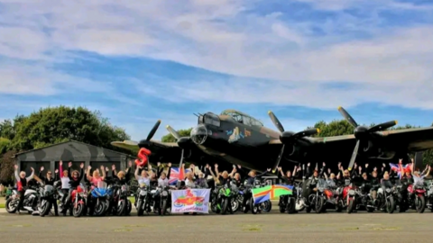 A large group of female motorcyclists on their bikes have a photo taken with a vintage RAF plane. 