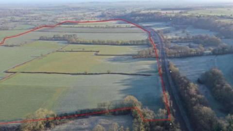 A drone shot of fields and countryside, a large red line drawn round the fields where solar panels would be 