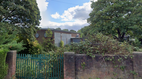 A derelict school building surronded by overgrown vegetation