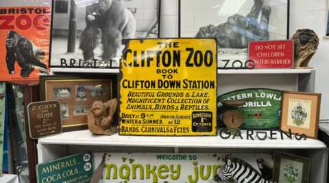 A yellow enamel zoo sign surrounded by other zoo memorabilia such as zoo signs, pictures of gorillas and mini gorilla statues