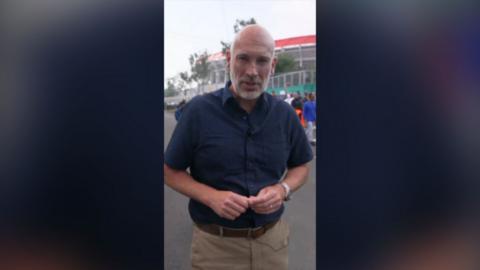 BBC Sports Editor Dan Roan stood in front of a stadium. He's wearing a navy shirt and beige trousers.