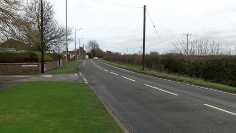 View of Staithes Road in Preston which has a single carriageway in both directions and a hedge bordering a field on one side with housing on the other side