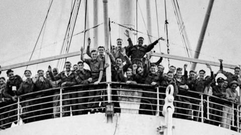 A black and white photograph of the HMT Empire Windrush with people from the Caribbean on board. They are gathered at the front of the ship and waving as it arrives at Tilbury in Essex.