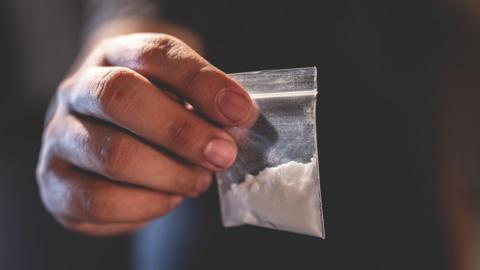 A bag of white powder is held in a man's hand.