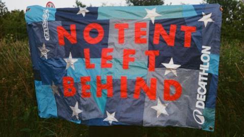 A blue chequered flag in different shades of blue, decorated with white stars and large red lettering reading ‘No tent left behind’ 