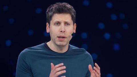 Sam Altman hearing a headset microphone on stage at an event