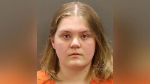 A mug shot of a young woman with blonde hair who stares at the camera