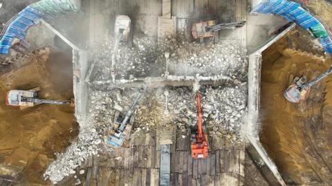 Aerial view of a motorway showing a huge rubble mess where a bridge has been knocked down.