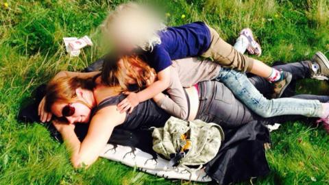 A woman lying face down on grass with two children lying on her back in a playful way.