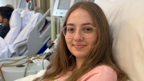 Sophie wearing a pink top and lying on a bed as stem cells are removed from her blood by a machine she is connected to. The Apheresis machine extracts the cells which she is donating to a stranger