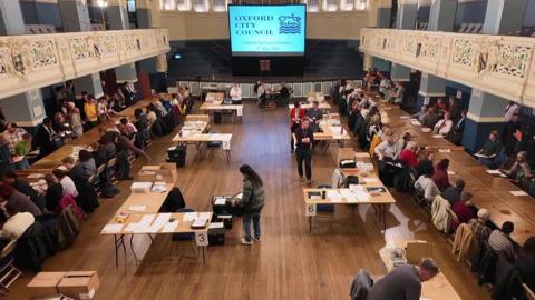 Oxford City Council election count in Oxford Town Hall. There are tables full of ballot papers that people are counting through.