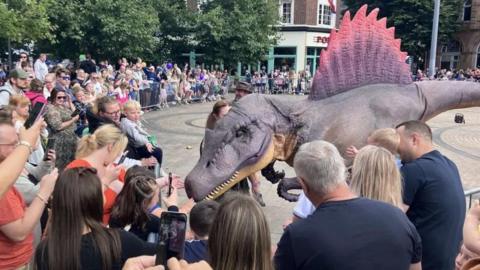 A female park ranger character talks about dinosaurs while posing with a Spinosaurus for the crowd.