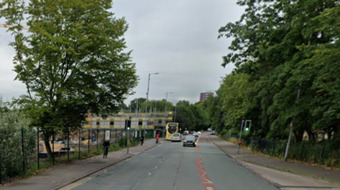 A yellow bus and cars drive down Rochdale Road near the crash site