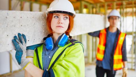 A young female builder carrying a stone slab