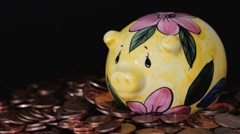 A yellow, pink and green piggy bank sitting on a pile of copper coins