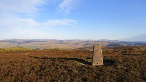 A trig point marker on top of a hillside in the Southern Uplands