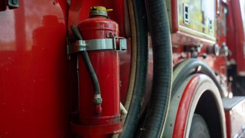 A close-up of the side of a fire engine. The red vehicle's black water hose can be seen, just in front of a wheel arch. 