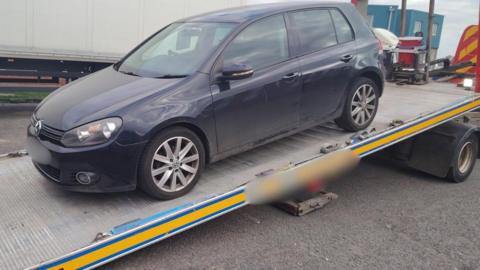 A dark coloured car on a ramp. It is being removed from a street.