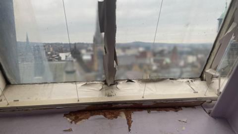 An old crumbling window frame looking out high above buildings in Sheffield