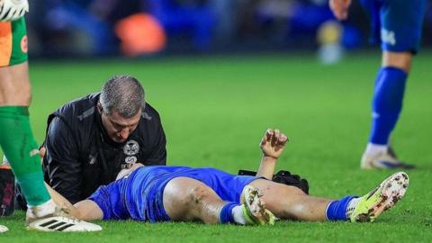 Harry Leonard, lying on the ground, is treated by a member of Peterborough United's medical staff