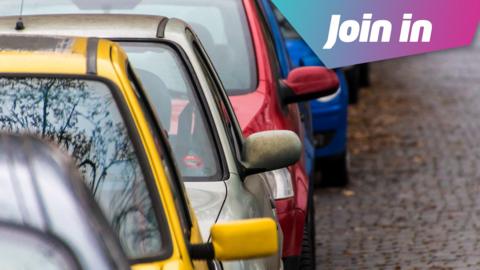 A line of cars in different colours. Yellow, then silver, then red and blue behind that. They are parked on the side of the road. 