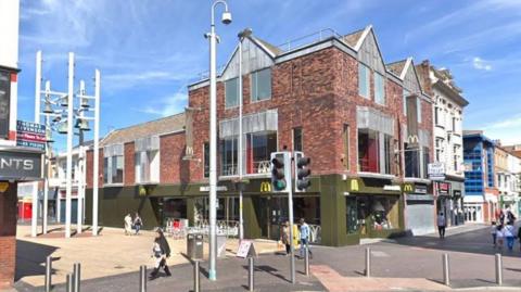 A Google Street view image of McDonald's. The Cleveland Centre is opposite and there are people walking about. It is sunny.