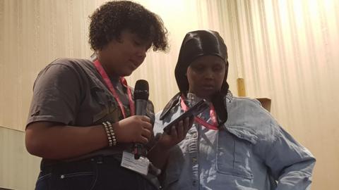 A young woman on the left stands beside her mother holding her mobile phone while reading a statement in front of the council.