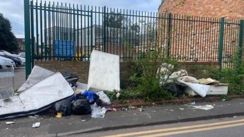 Fly-tipped rubbish on a street near a doctors' surgery. The dumped waste includes a white mattress and black rubbish bags.