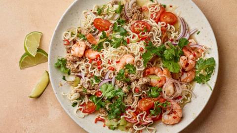 A white plate filled with curly noodles, prawns and herbs on a beige background