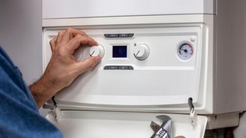 A person's hand turning a dial on a white boiler