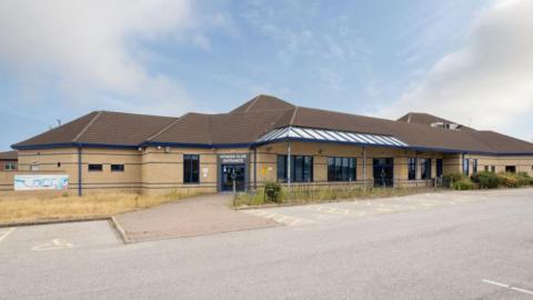 Front view of the brick-built single-storey building. There is a fitness club sign above the door and an advertising banner to the side of the building.