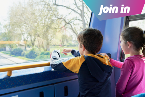 A boy and a girl look out the front of a bus window.