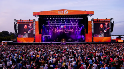 A festival stage watched by a crowd. Belinda Carlisle is performing