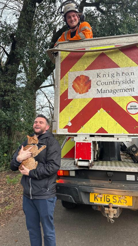 Knighton Countryside Management worker in a cherry picker vehicle parked behind Elliott Sawyer who is holding Otto the cat