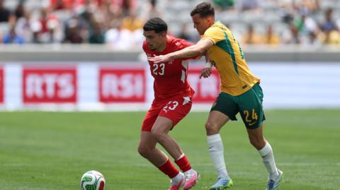 Zeki Amdouni, wearing Switzerland's red home kit with white accents, competes for the ball against Australia's Paul Okon-Engstler on 6 June
