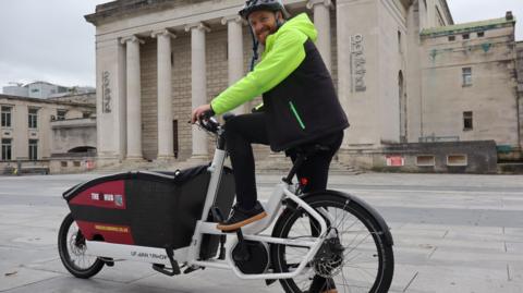 A man in a black and yellow hi-vis jacket on an e-bike delivering books from Southampton Central Library as part of a new trial.