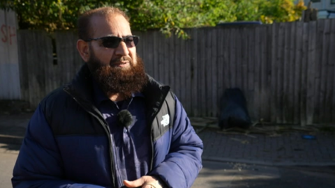 Image shows Mahmood Iqbal in a road in Lozells wearing a blue coat