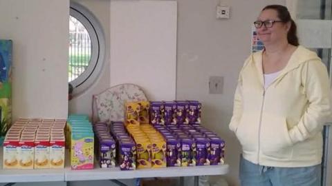 Margo Bohacz standing next to dozens of chocolate Easter eggs lined up on a table.