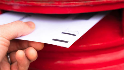 A white letter is put into a red letterbox in a close-up image.