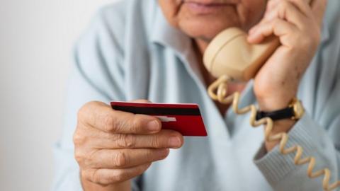 Image of somebody on the phone whilst looking at their bank card