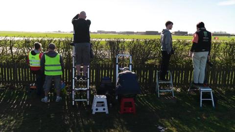 Plane spotters stand on ladders by the runway at RAF Waddington