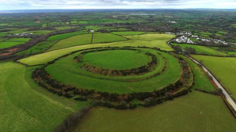 A drone shot of the circular fort. It is grassy and surrounded by numerous fields.