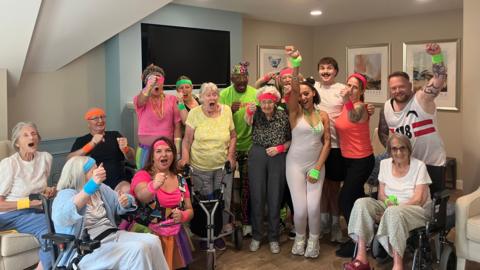 Care home residents and staff at Lindley Park pose for a photo with Mr Motivator while wearing bright-coloured head and wrist bands.