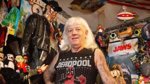 Man with white hair standing next to a 6ft Terminator
