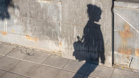 Shadow of a child on the concrete as they walk down the street, looks like they are wearing a rucksack and are on their own