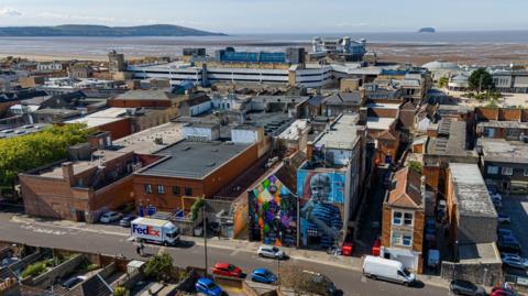 A view over Weston with the beach in the background. There is some colourful artwork on some of the house walls in the foreground of the picture.
