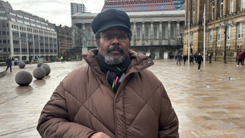 Pictured is Bishop Jaddoo wearing a black hat, glasses and a brown buffer jacket in Victorian Square.