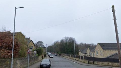 A picture of a road with houses and cars parked on both sides of the road