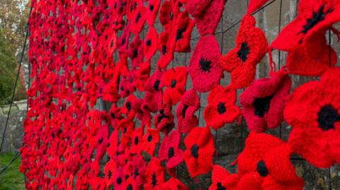 Hundreds of red knitted poppies that have been woven together attached to webbing on the side of the church building. 